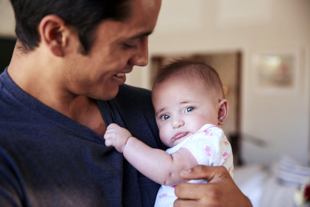 Millennial Hispanic father holding newborn son, baby looking to camera, head and shoulders, close up